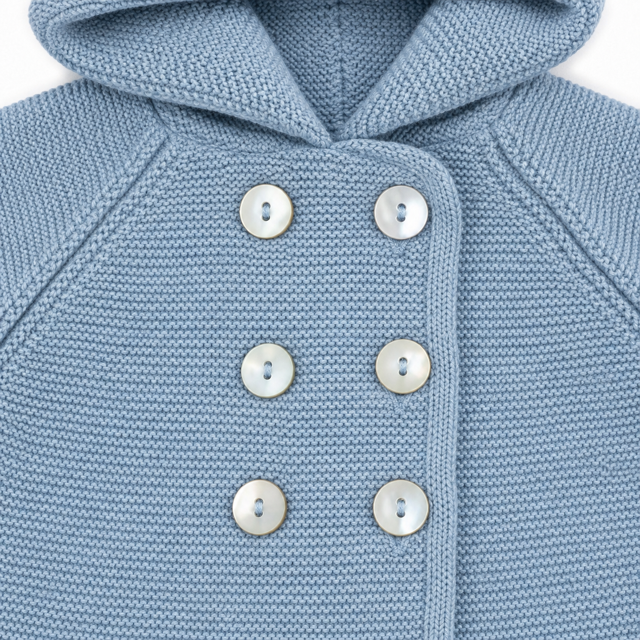 Detalle en primer plano de la capucha integrada, la textura del punto y los botones nacarados delanteros de la chaqueta San Francisco en color azul empolvado.