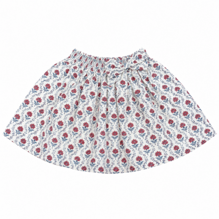 Vista frontal de la falda infantil con estampado floral de flores rojas y hojas azules, cintura elástica fruncida y un lazo decorativo lateral para niñas de 4 a 8 años, producto elaborado en España.